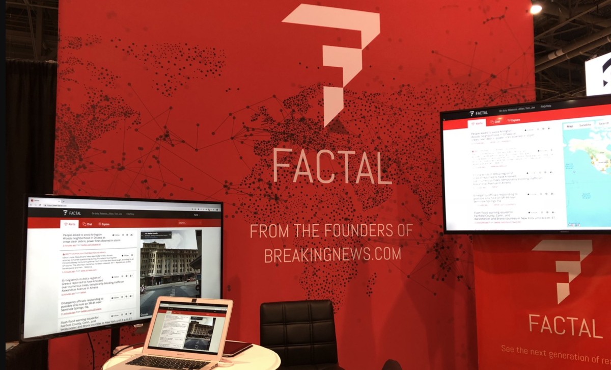 Factal's first booth at GSX. Three screens of varying sizes with Factal's web platform pulled up on each. At back, a red step-and-repeat with the Factal logo and tagline "From the founders of Breakingnews.com" over a map of the world where cities are represented by dots and connected by black lines.