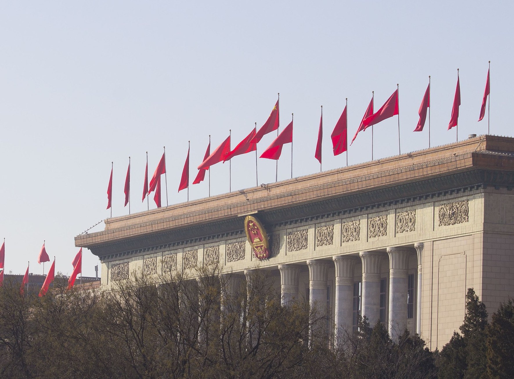 Great Hall of the People in China with more than a dozen flags flying against a sky without clouds