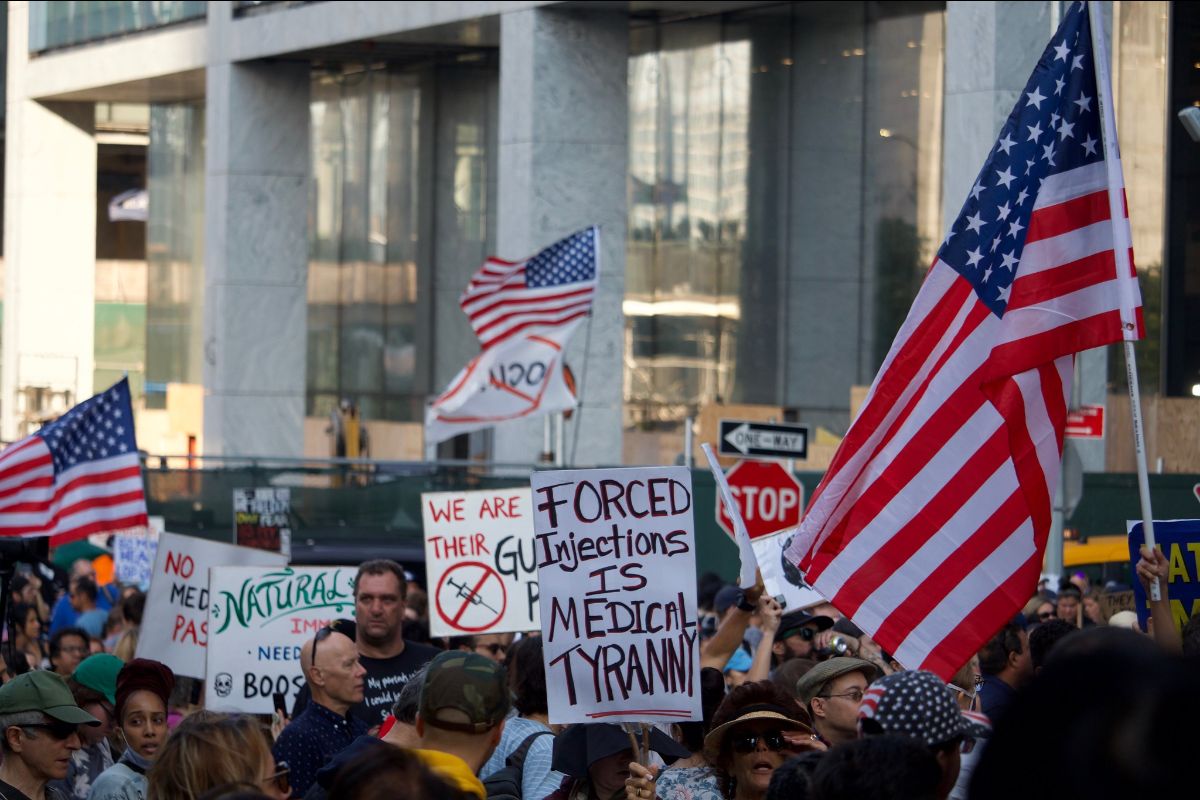 Signs and American flags are visible in a crowd on a downtown street.