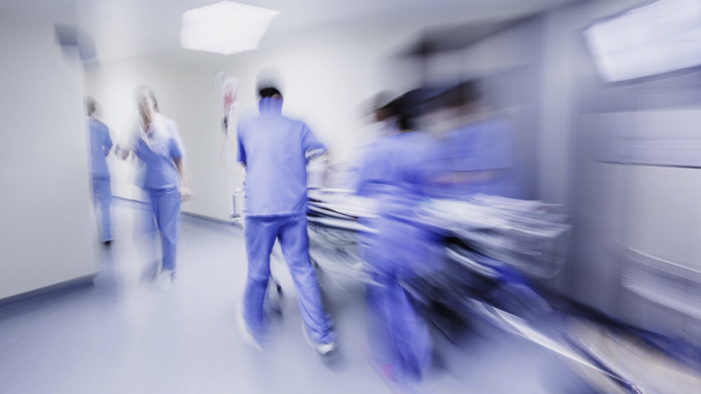 Doctors and nurses rush a cart through a hospital hallway