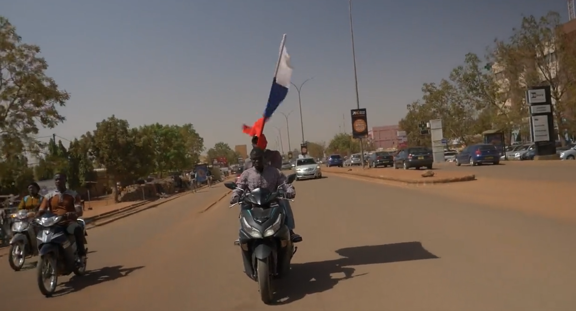 Screencap from a video by Henry Wilkins of "Two pro coup demonstrators seen flying a Russian flag through the streets of Ouagadougou" on January 25, 2022.