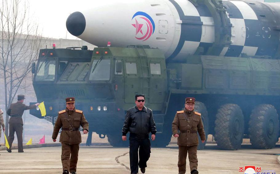 Kim Jong Un walks in front of an ICBM. He is flanked on either side by two men in military uniforms.