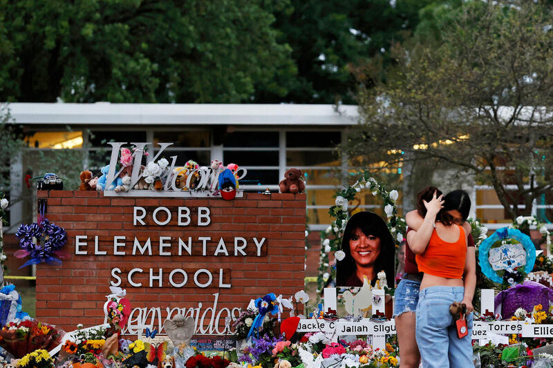 A detail view as people embrace outside a memorial to honor the victims killed in this week's school shooting outside Robb Elementary School. A makeshift memorial filled with flowers and photos of the 21 victims in honor of the victims, most of whom were around 10 years old. President Biden traveled to Uvalde, Texas, to help console the community as it grieves from, and seeks to comprehend, last week's massacre at Robb Elementary School.