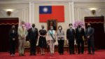 Nine political leaders of the United States and Taiwan pose in formal presentation. In the center are Nancy Pelosi and Tsai Ing-wen. Behind them is the flag of Taiwan. They stand on a red carpet.