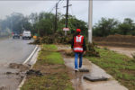 An aid worker with American Red Cross vest on, walks down a rainy sidewalk that is blocked by debris from Hurricane Fiona