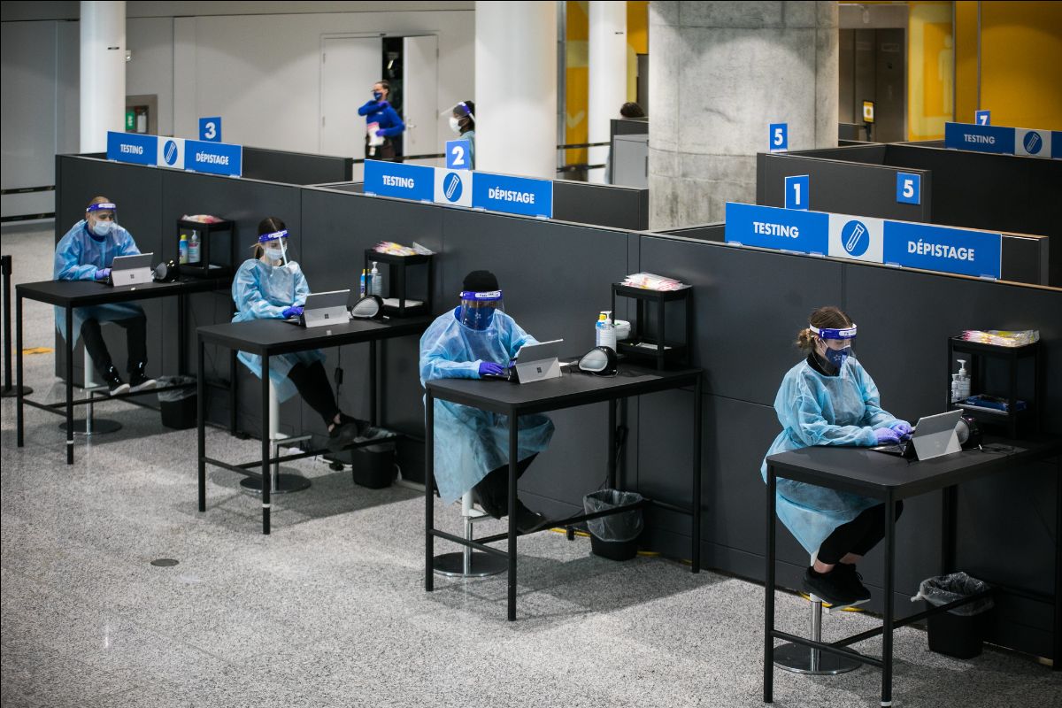 A photo of a coronavirus testing facility in Toronto. There are four people in protective gear seated at desks waiting for tests subjects.