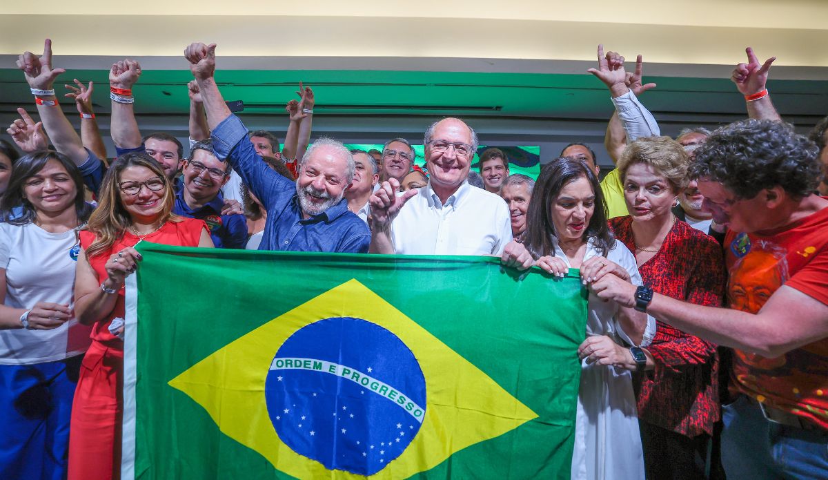 Brazil's former President Luiz Inácio Lula da Silva celebrates victory with dozens of supporters. da Silva's companions are holding the flag of Brazil in front of him.