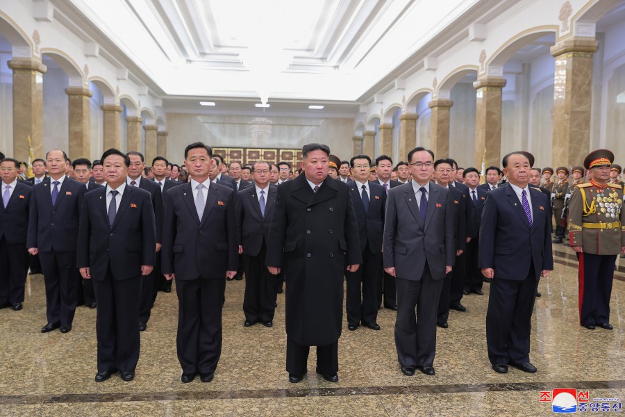 North Korean leader Kim Jong Un stands in front of dozens of other men. All are in suits.