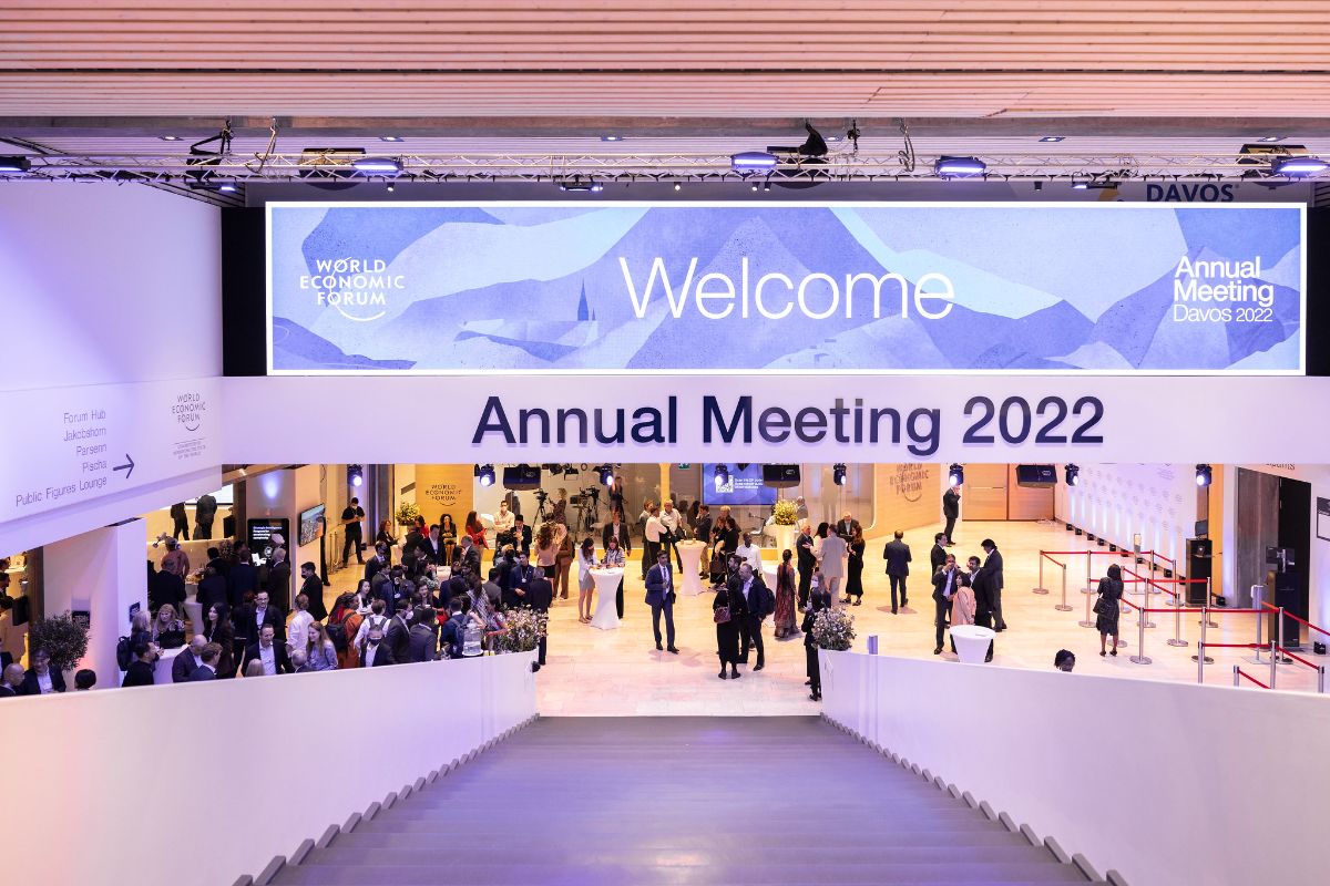 Dozens of individuals in various suits stand in front of the welcome banner and entry to the 2022 World Economic Forum