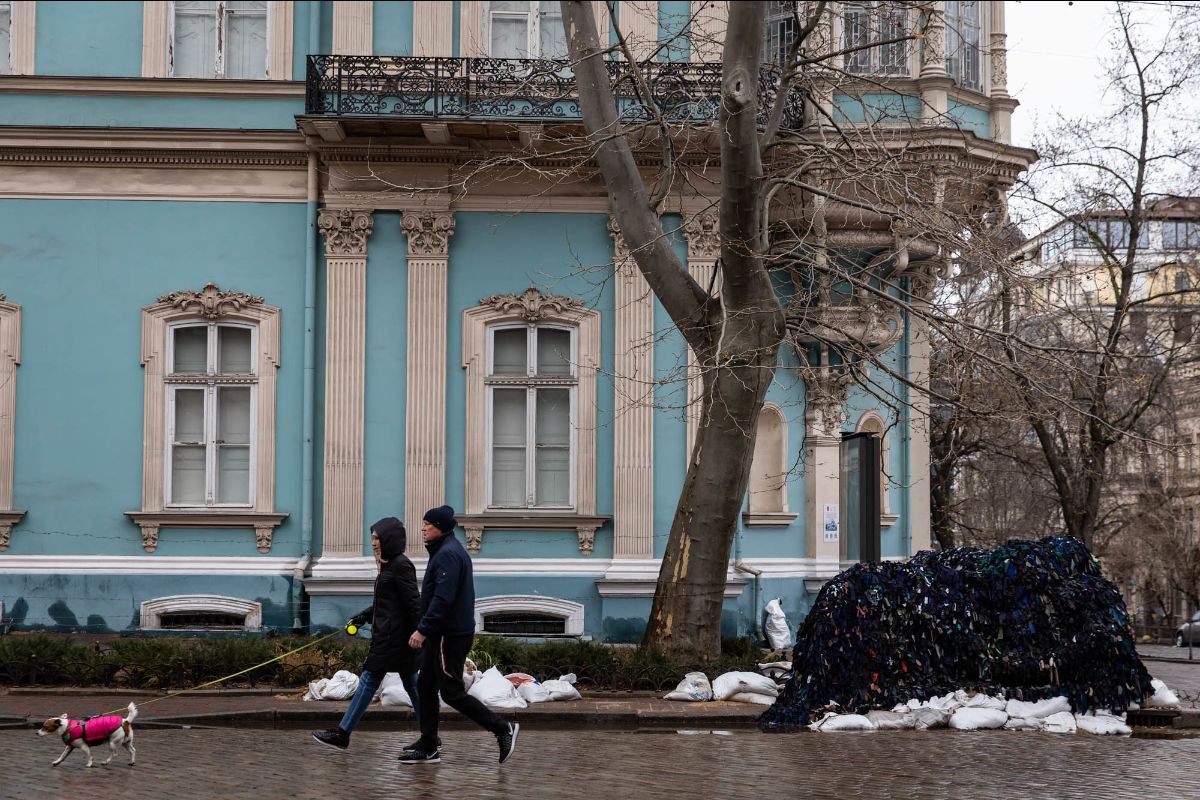 On a street in Kyiv two people walk their dog in front of a pale blue building