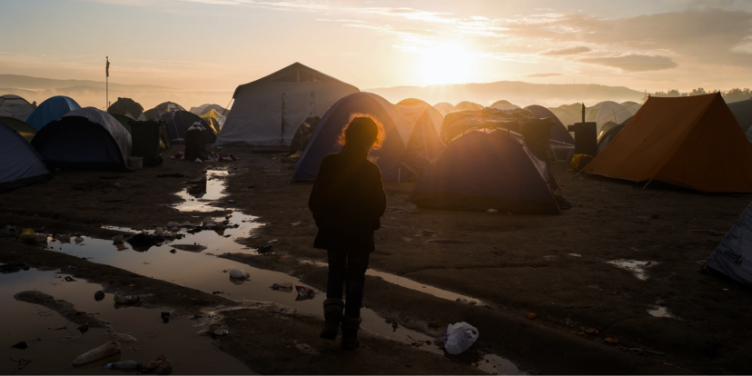 Several camping tents surround an aid tent at sunrise. There is a person looking at the camp
