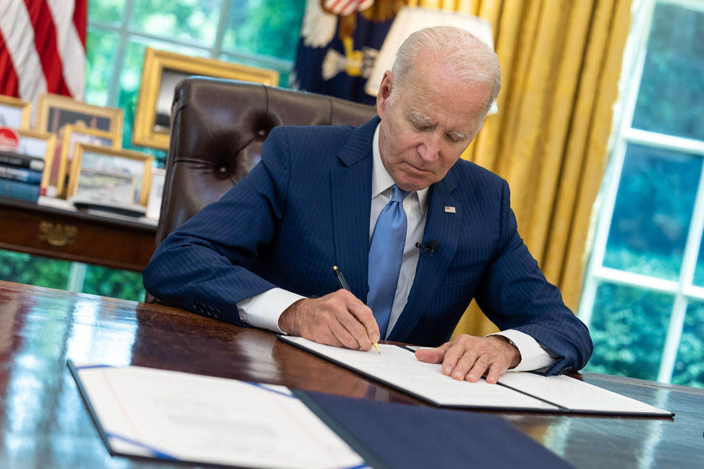 U.S. President Joe Biden is signing a paper in the Oval Office. This photo is a close up of the action of signing.