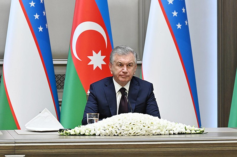 Uzbekistan President Shavkat Miriziyoyev sits at a desk with flags behind him.