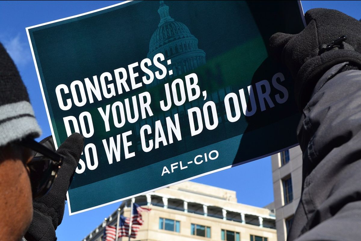 A sign held in the air that says "Congress do your job so we can do ours"