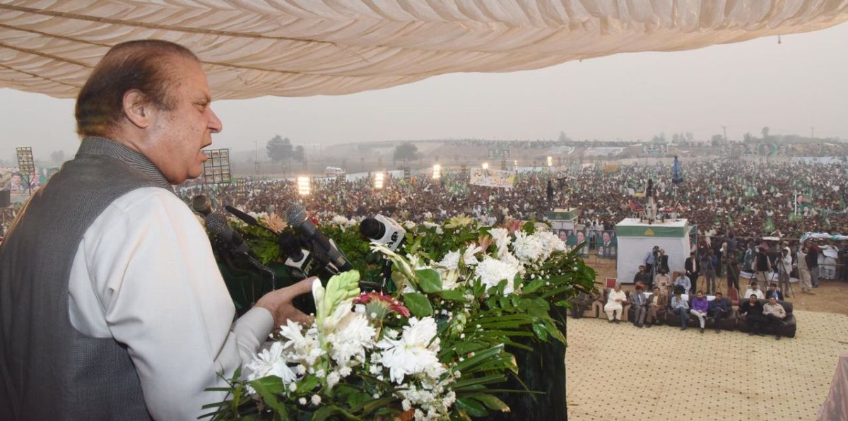 Nawaz Sharif is on a balcony overlooking a large crowd in a city with low buildings.