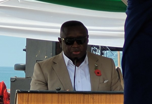 Sierra Leone President Julius Maada Bio stands at podium with sunglasses on. There are curtains in the colors of the national flag behind and above him