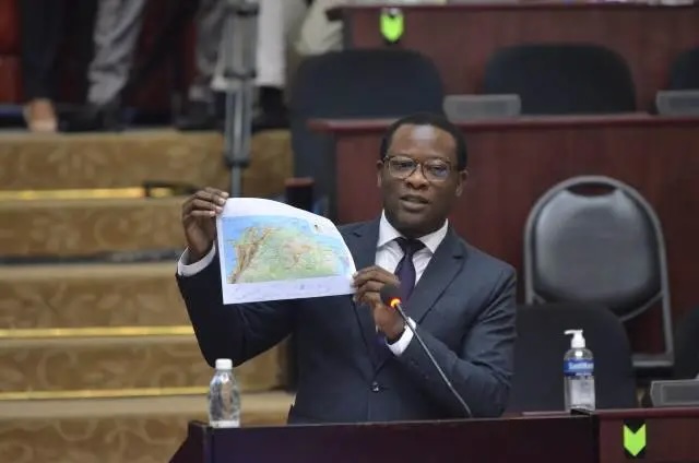 A man holds up a printed map of the northern portion of South America as he presents in lecture hall or speaking room.