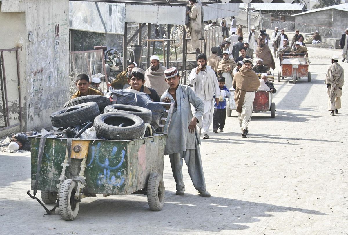 Pushing a large three-wheel cart are three males in working clothes