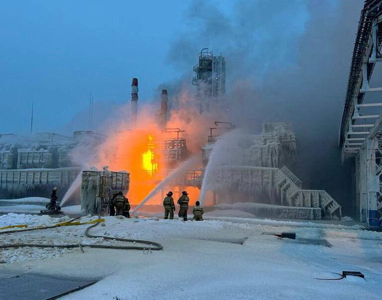 In snow and ice there is a burning oil facility with a few firefighters trying to extinguish the flames