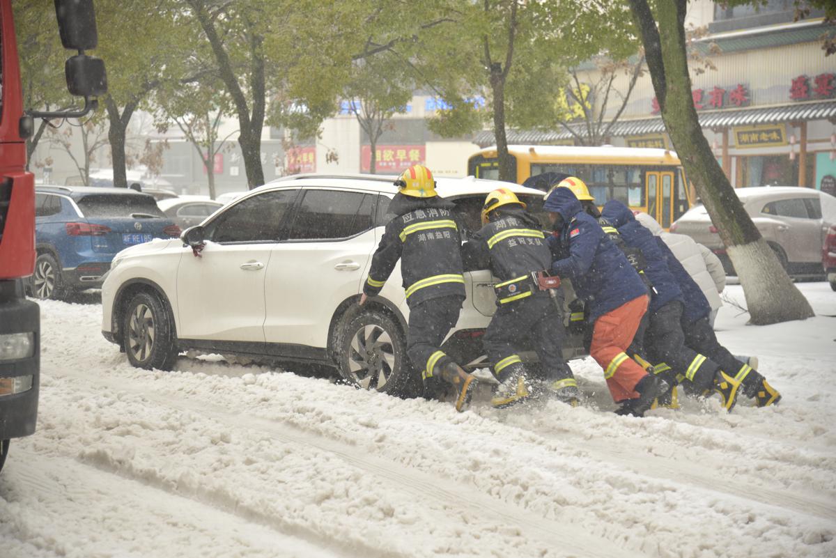 Five first responders push a small SUV through snow of about 4 inches.