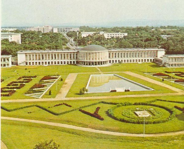 Aerial view of a landscaped garden with a central building featuring a dome, a large reflecting pool, and geometric hedges.