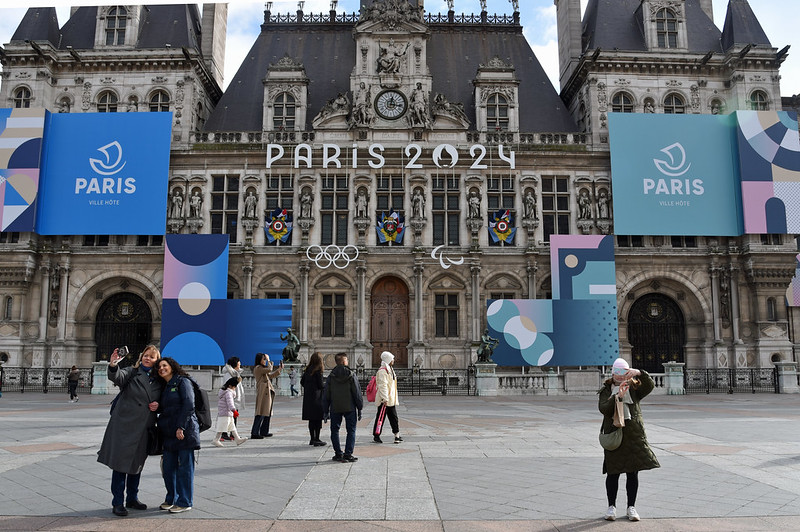 Paris City Hall with Paris 2024 Olympics banners and people in the plaza.