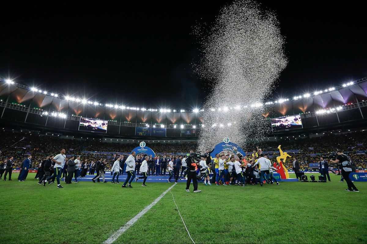 Celebration on the field with confetti in a stadium at night. A group gathers around the CONMEBOL Copa America stage.