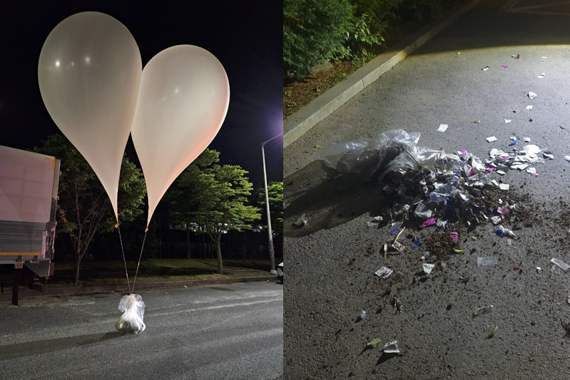 Two large white heart-shaped balloons tied to a weight on one side; scattered trash on an asphalt surface on the other.