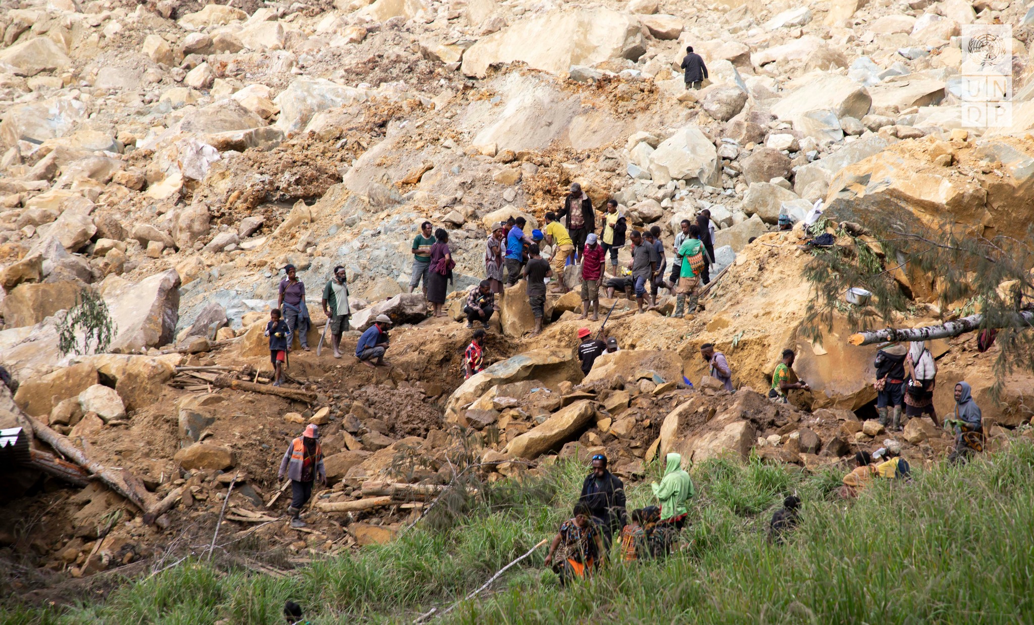 A group of people working in a rocky terrain with large boulders and some grassy areas in the foreground. "UNDP" logo in the top right corner.