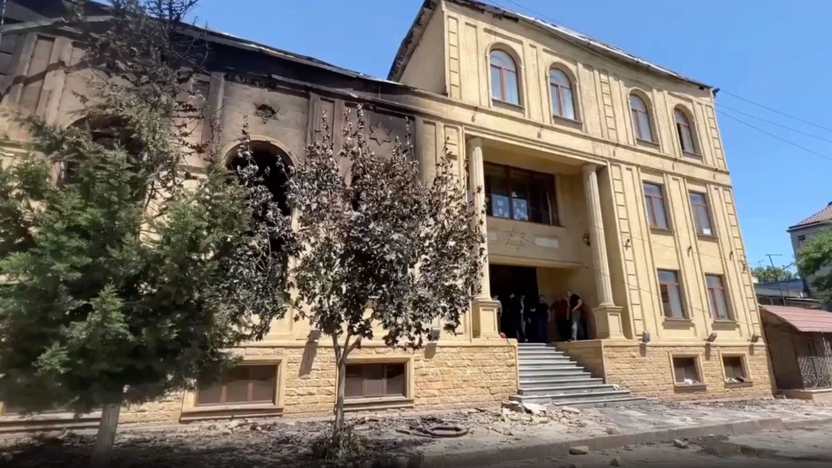 A damaged beige building with fire damage and debris on the ground, featuring a wide staircase and columns at the entrance.