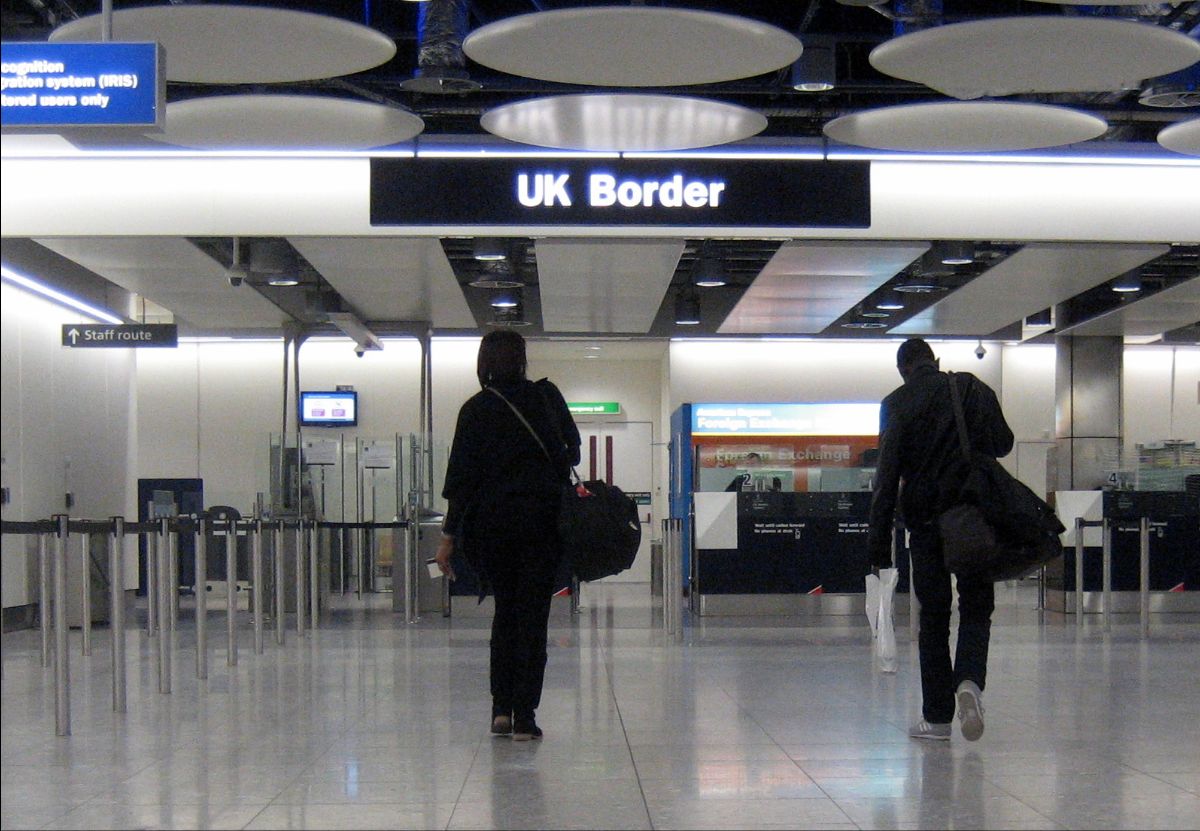 Entrance to UK border control area with two people walking towards the automated gates.