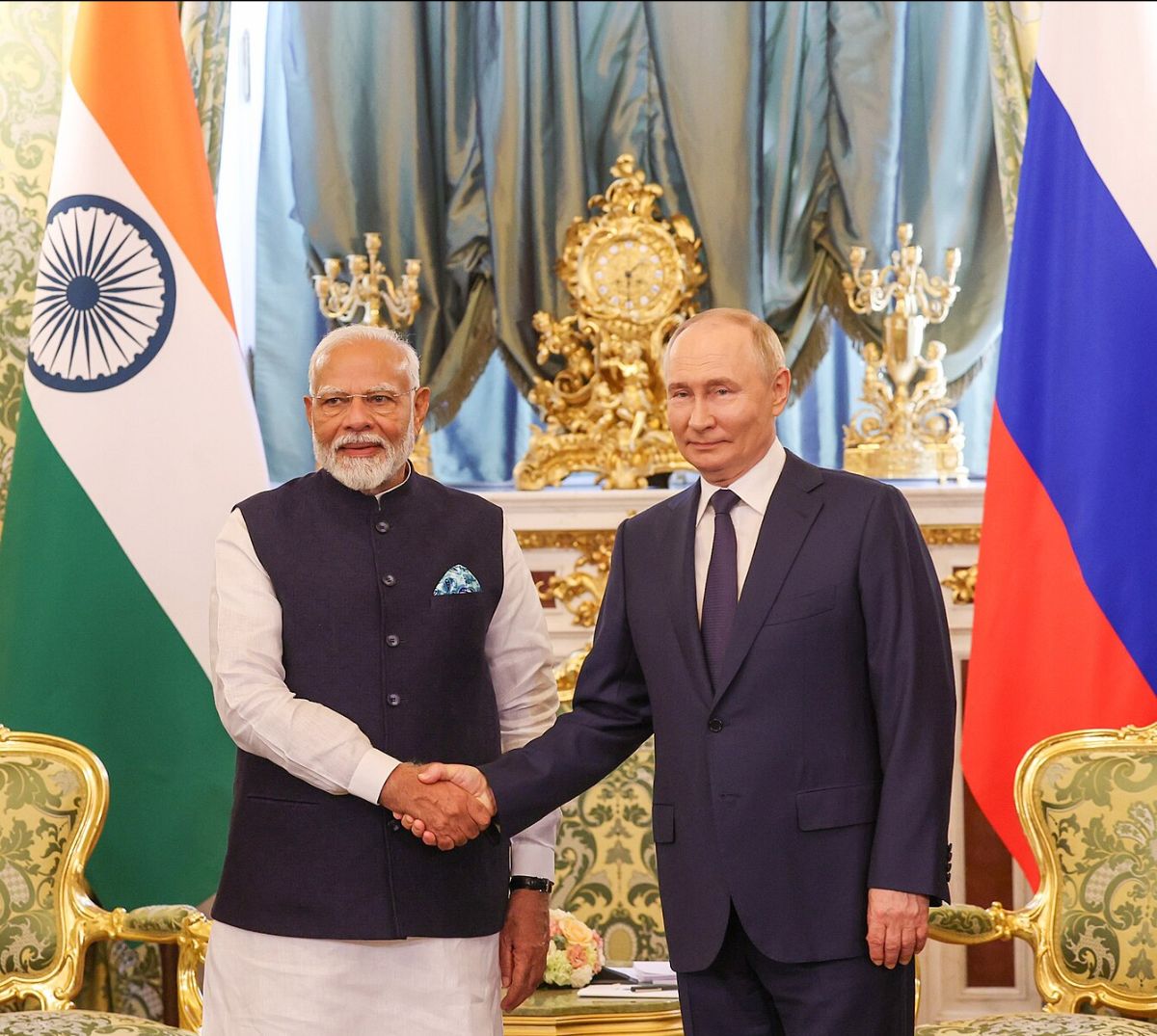 Two men shake hands in an opulent room with Indian and Russian flags beside them.