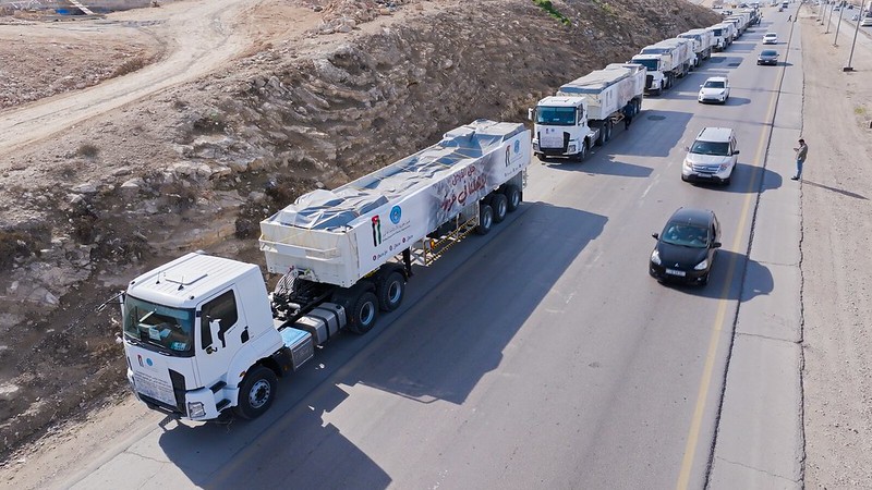 Photo of aid trucks on a desert road being inspected by a single person