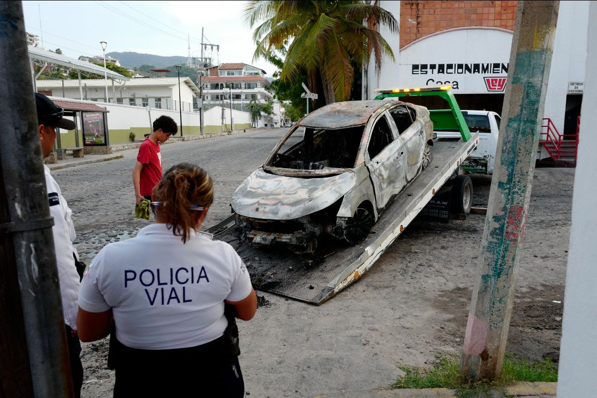 A burnt car being loaded onto a tow truck, with police officers observing the scene.