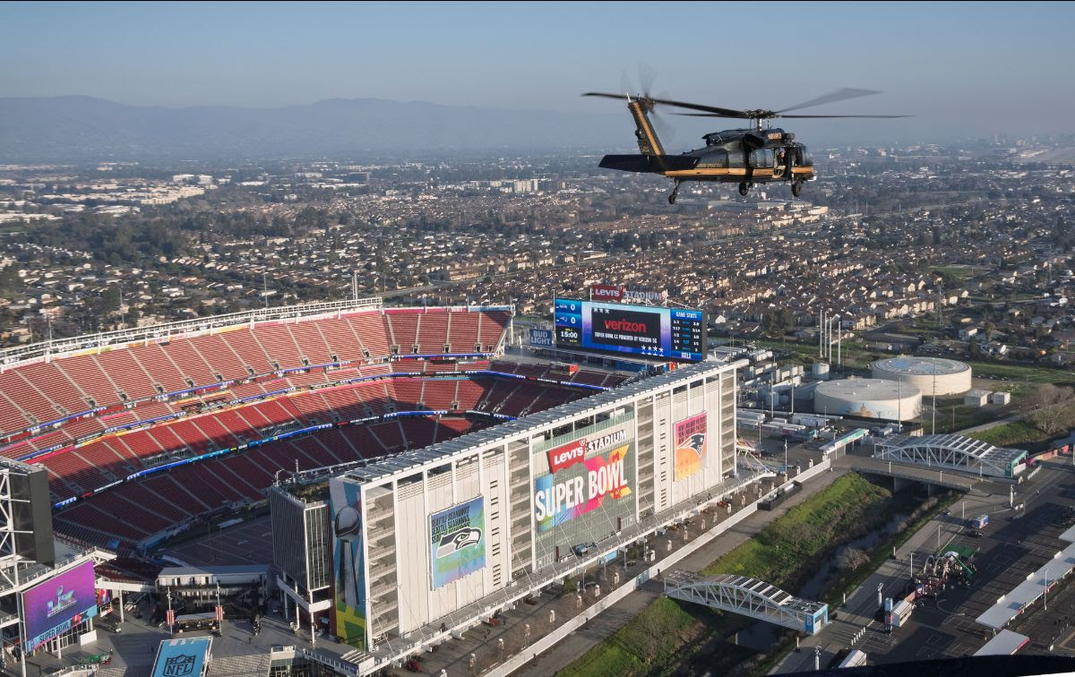 Aerial view of Levi's Stadium hosting the Super Bowl, with a helicopter flying above and a cityscape in the background.