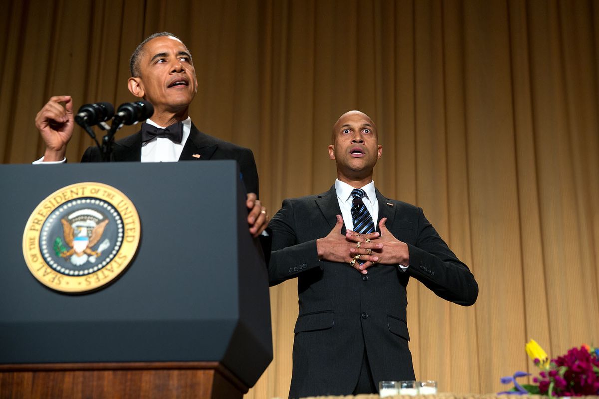 The image depicts a scene with two men wearing formal attire behind a podium adorned with the Seal of the President of the United States. The man on the left is dressed in a black tuxedo with a bow tie, standing at the podium, holding a gesture with his hand. The man on the right is also in a dark suit and tie, with a surprised facial expression, hands clasped together in front of his chest. The background features beige curtains, and there are floral arrangements at the bottom right corner.