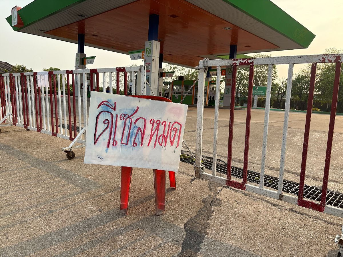 A barricaded entrance with a sign in Thai at a gas station.