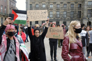People at a public rally holding pro-Palestinian signs and banners.